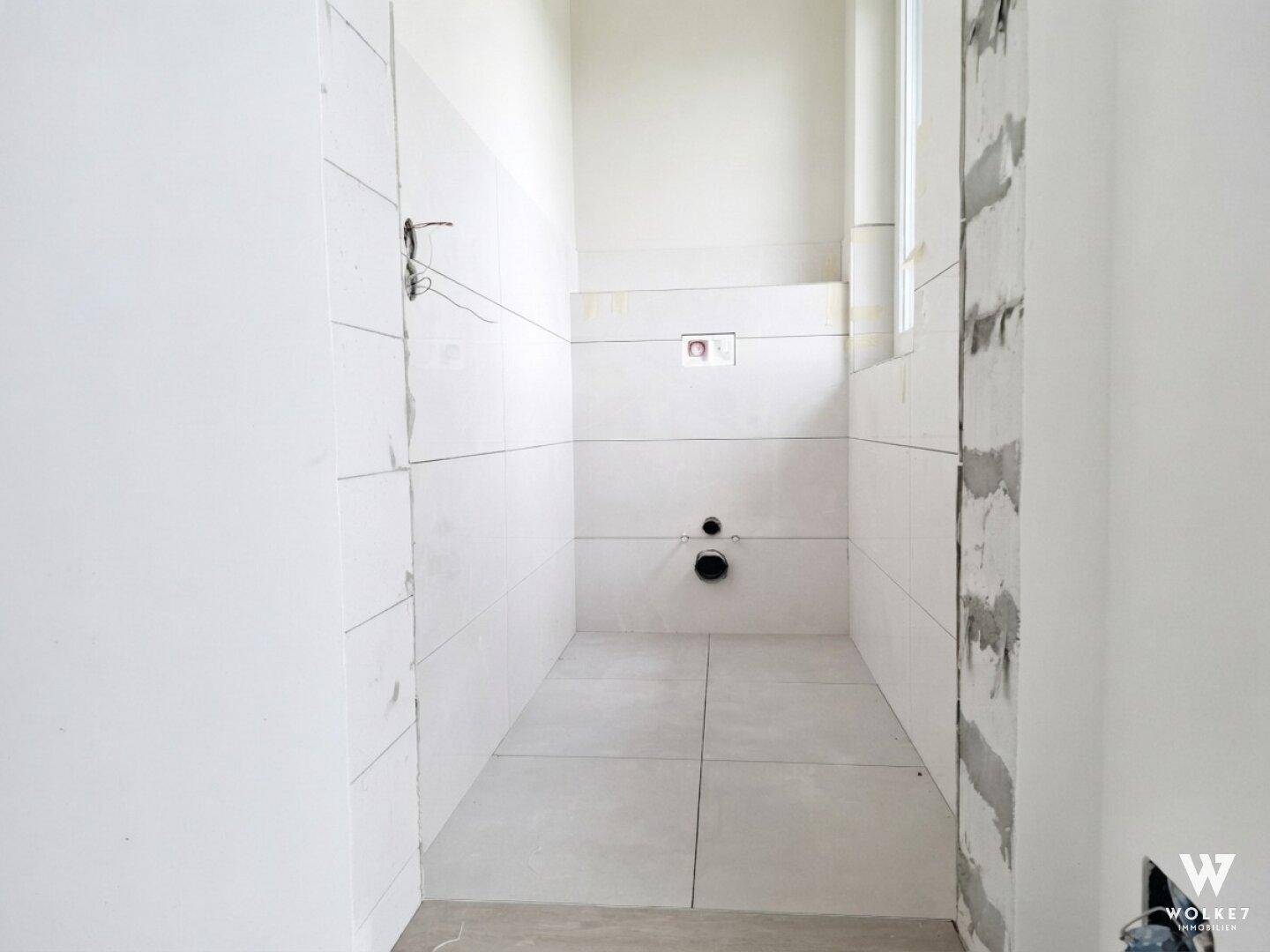 Unfertiges Gäste-WC mit weißen Fliesen und Vorbereitung für Wand-WC.