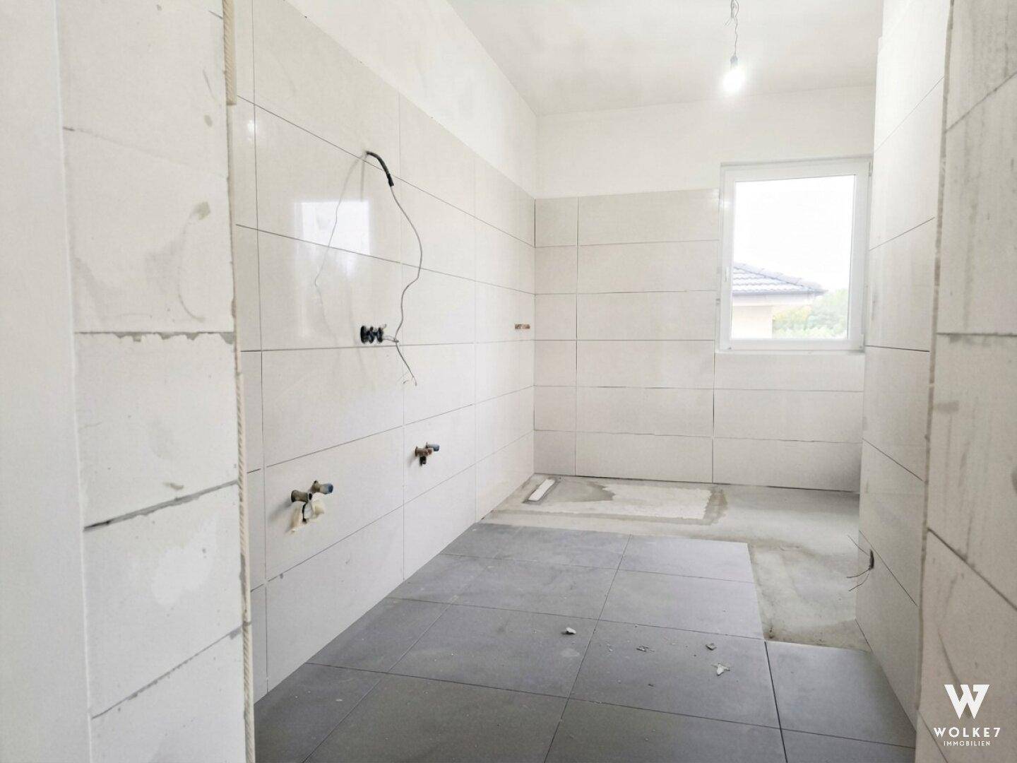 Helles Badezimmer im Rohbau mit weißen Wandfliesen und Fenster.