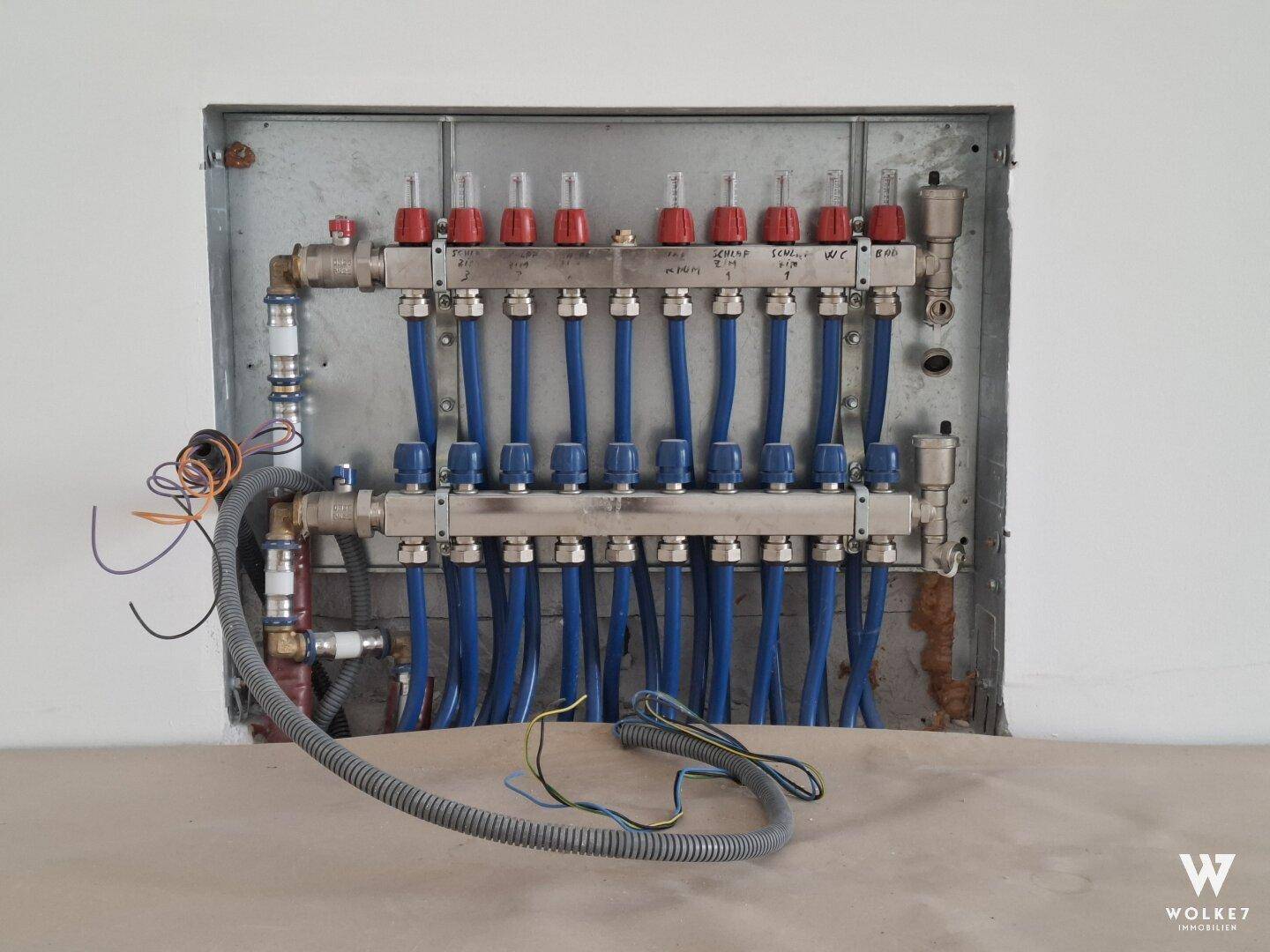 Verteiler für die Fußbodenheizung mit blauen Leitungen, installiert im Technikraum.
