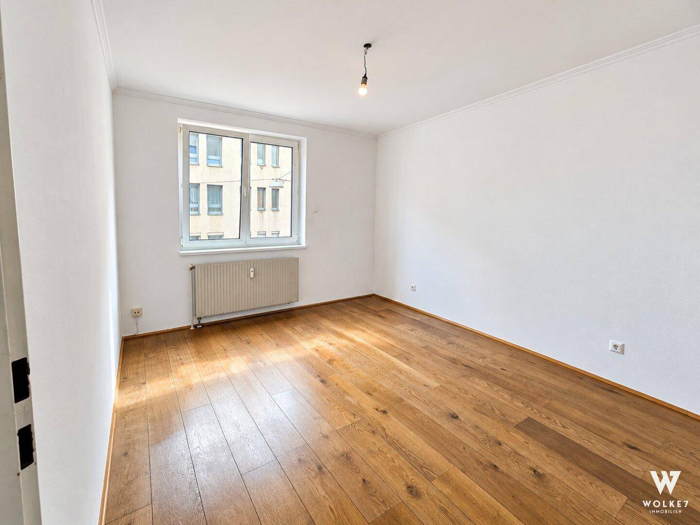 Helles Schlafzimmer mit Holzboden und Blick auf die umliegenden Gebäude in der Stadt.