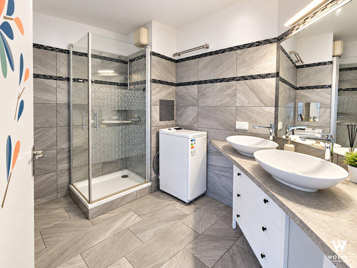 Modernes Badezimmer mit doppelten Waschbecken, begehbarer Dusche und einer Waschmaschine.