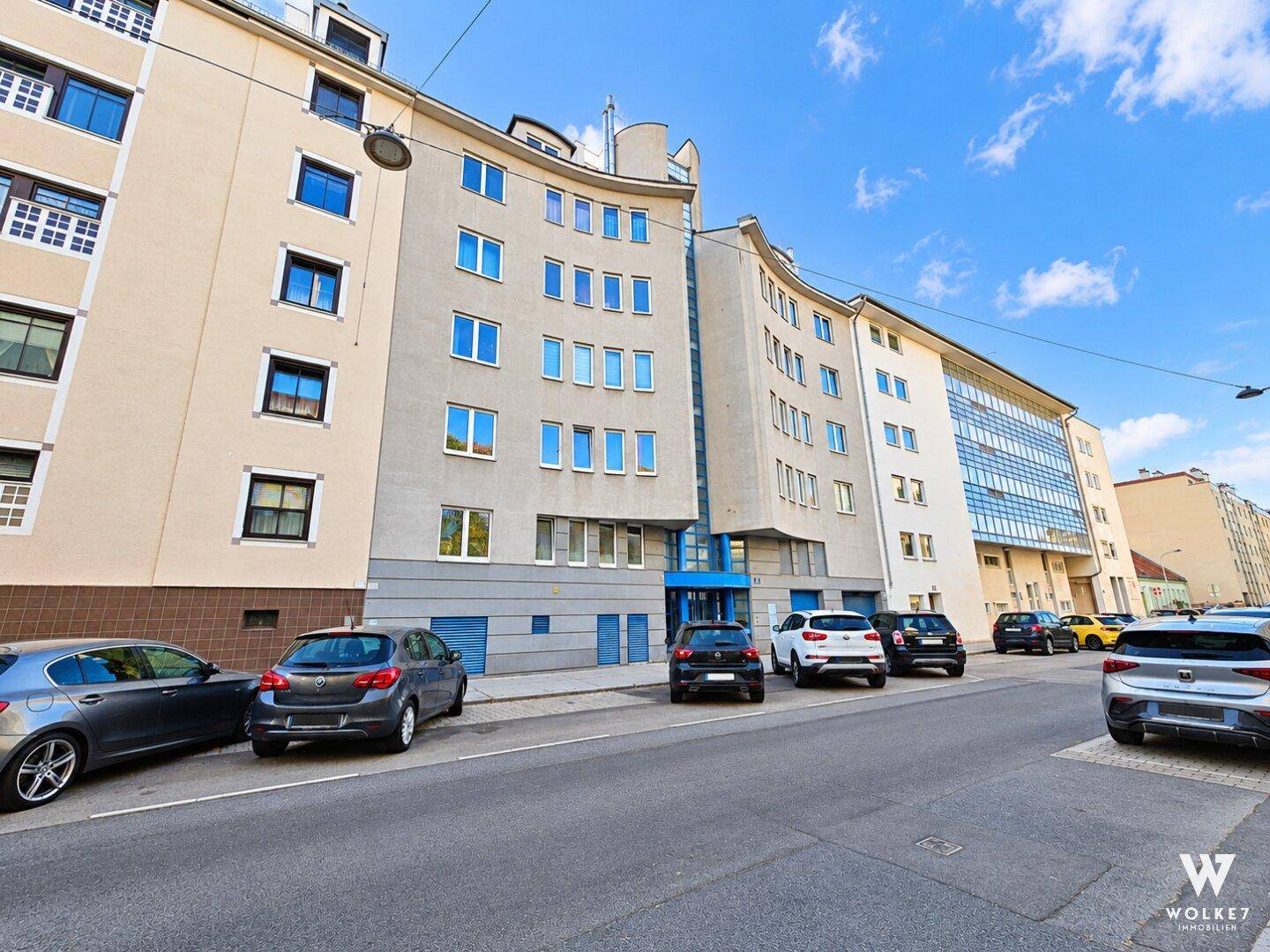 Mehrstöckiges Wohngebäude mit moderner Architektur und geparkten Autos auf der Straße.