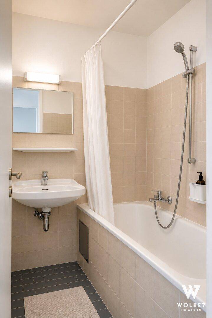 Badezimmer mit Badewanne, Duschvorhang und beigefarbenen Wandfliesen.