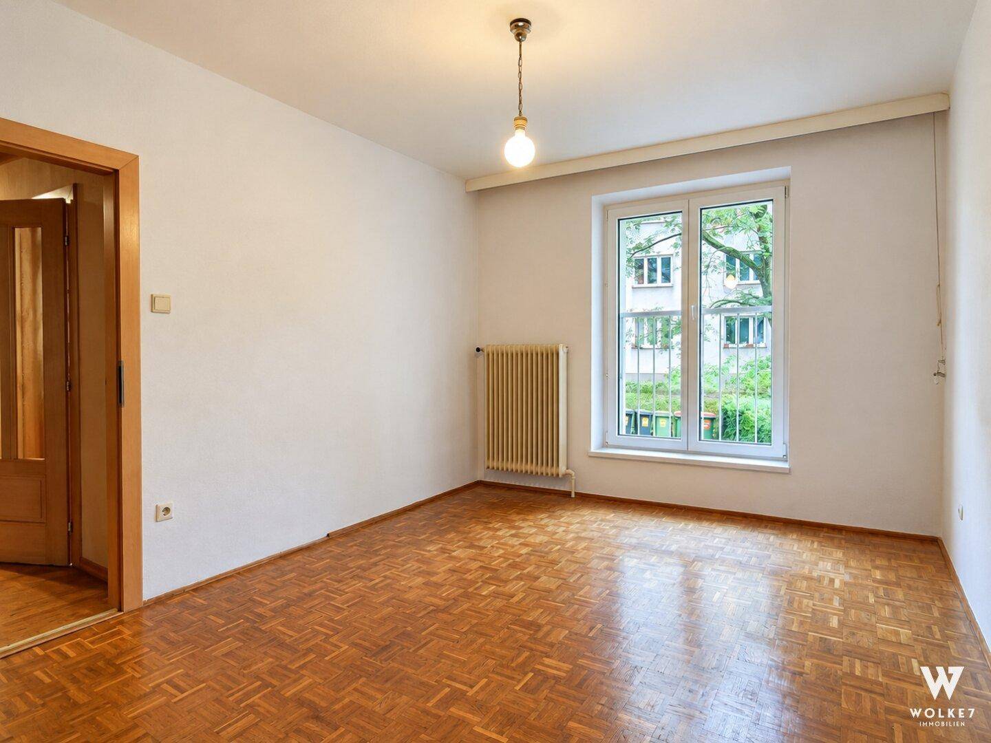 Leeres Zimmer mit Fischgrätparkett, weiß gestrichenen Wänden und Blick auf die Umgebung.