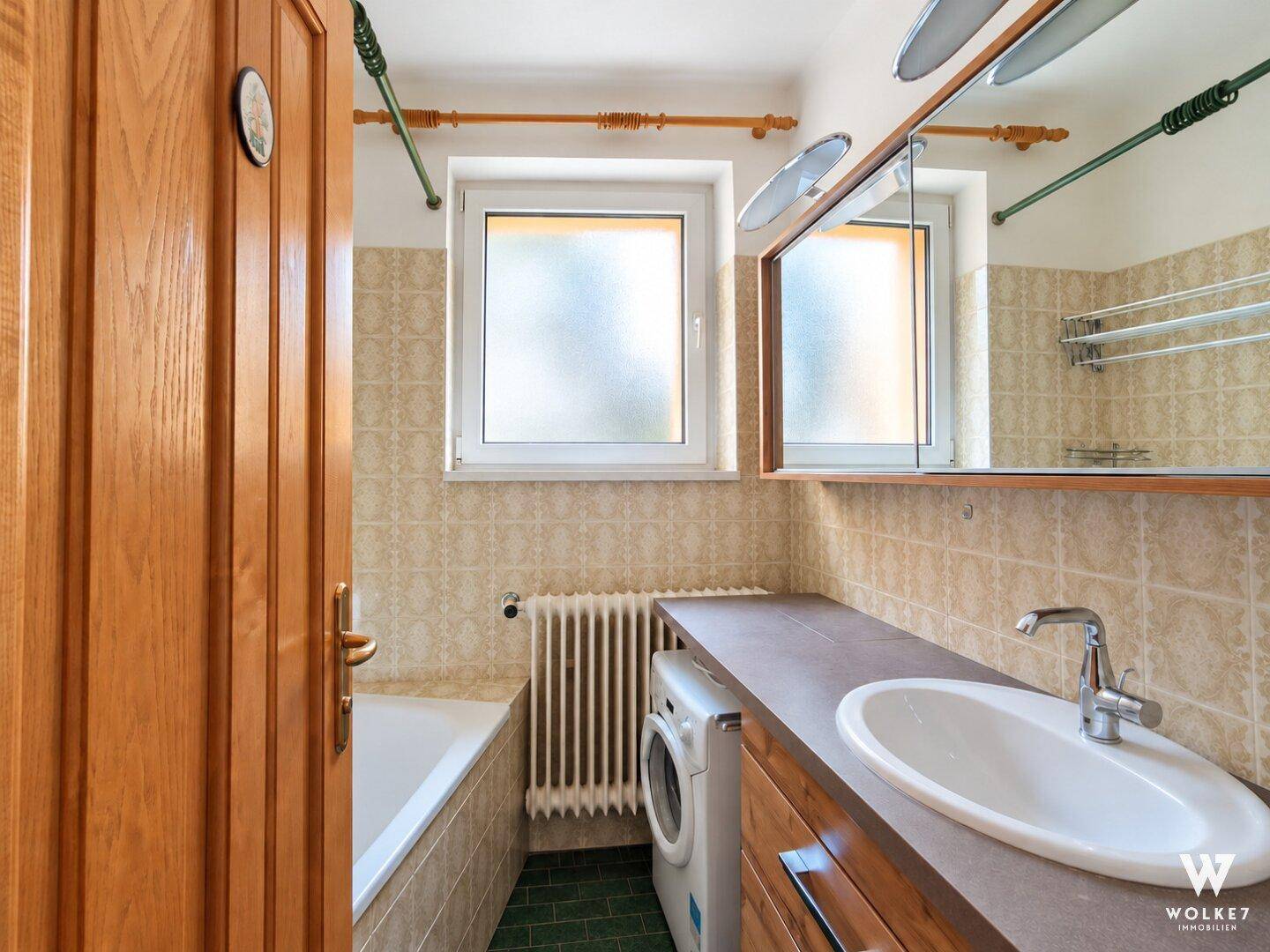 Badezimmer mit Badewanne, Waschbecken, Spiegelschrank und gefliesten Wänden.