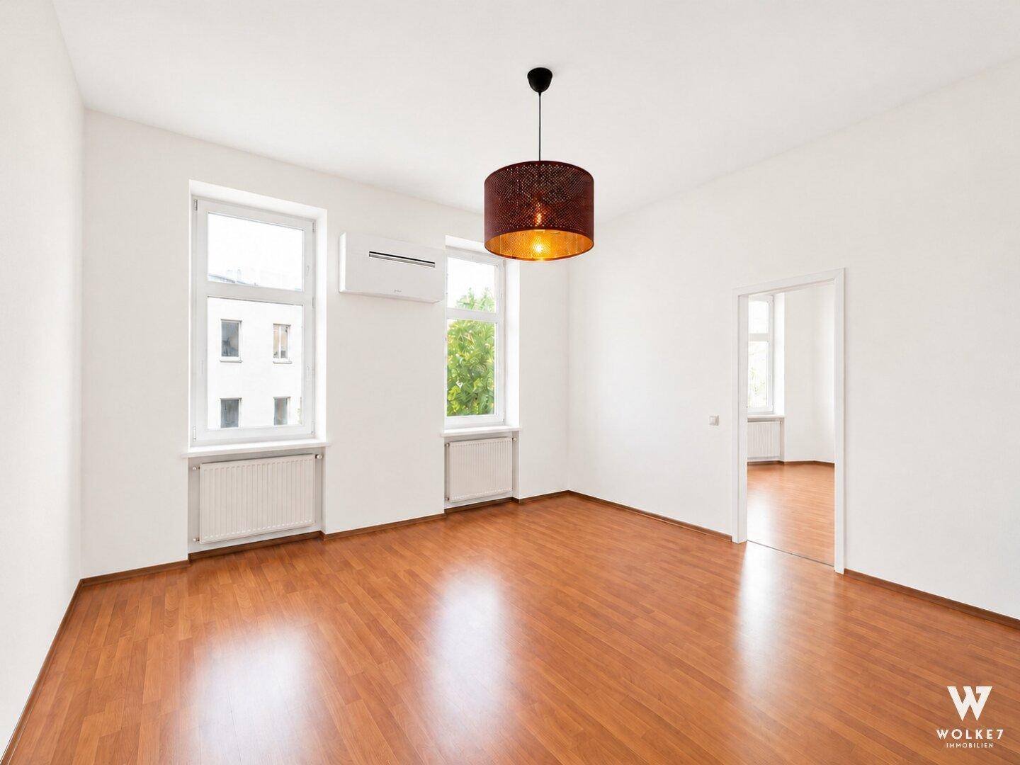 Geräumiges, leeres Zimmer mit Laminatboden, hohen Fenstern und einem modernen Deckenlicht.