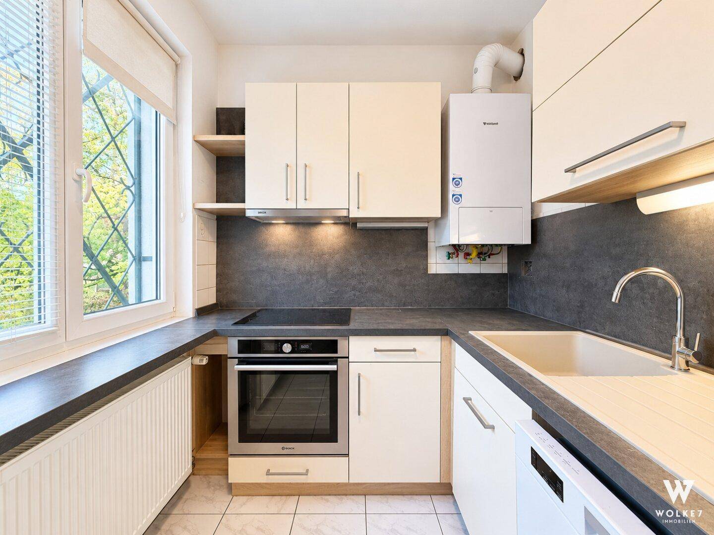 Funktionale Küche mit weißen Schränken, dunkler Arbeitsplatte und integrierten Geräten sowie einem Fenster.