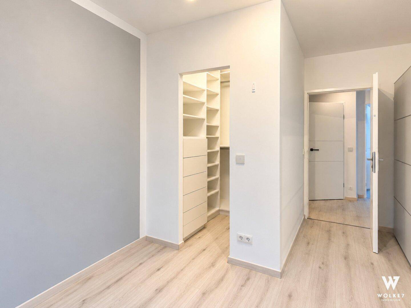 Schlafzimmer mit Zugang zu einem begehbaren Kleiderschrank und hellem Laminatboden.