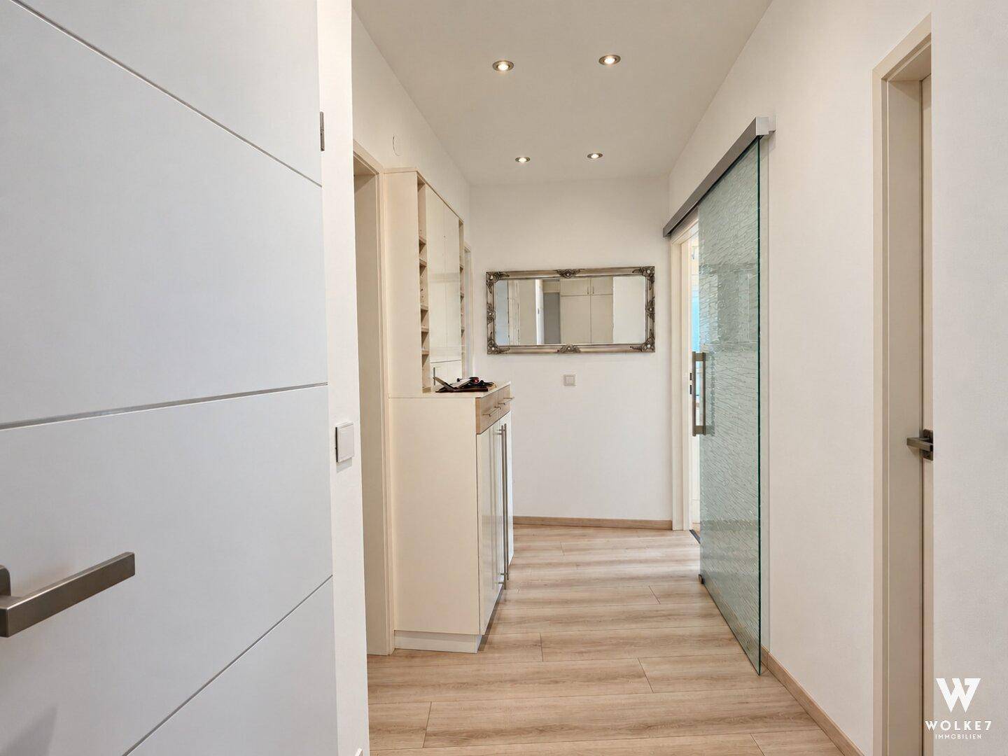 Heller Flur mit Laminatboden, Spiegelschrank und einer modernen Glasschiebetür.