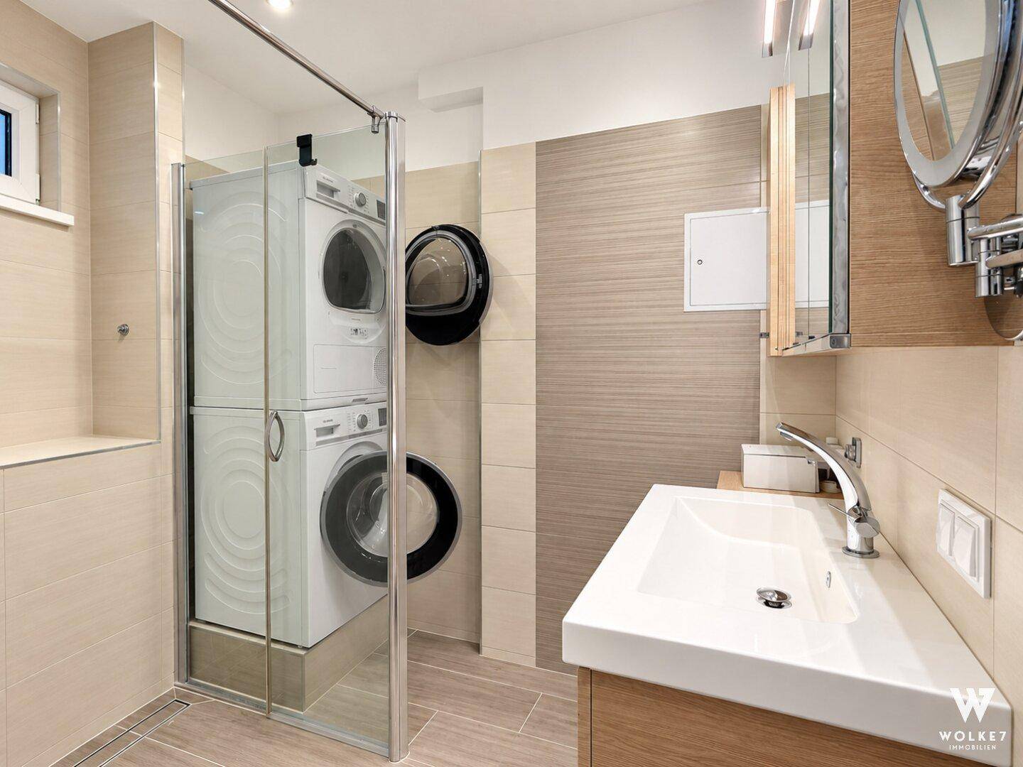 Modernes Badezimmer mit Dusche, Waschbecken und integrierter Waschmaschine und Trockner.