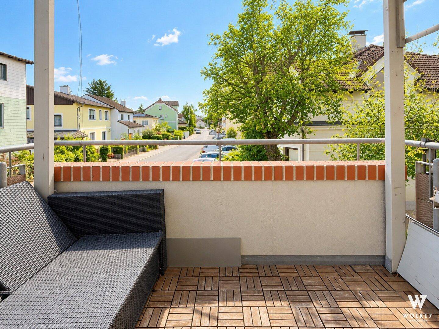 Balkon mit Holzbodenfliesen und Liegestuhl, bietet einen Blick auf die Wohngegend.