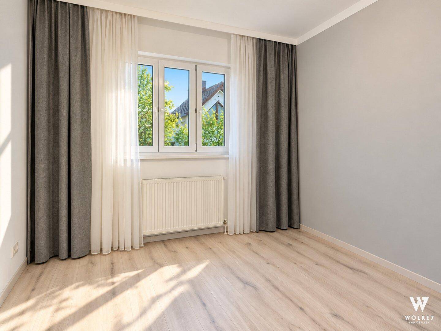 Leeres Schlafzimmer mit hellem Laminatboden, grauen Wänden und großem Fenster.