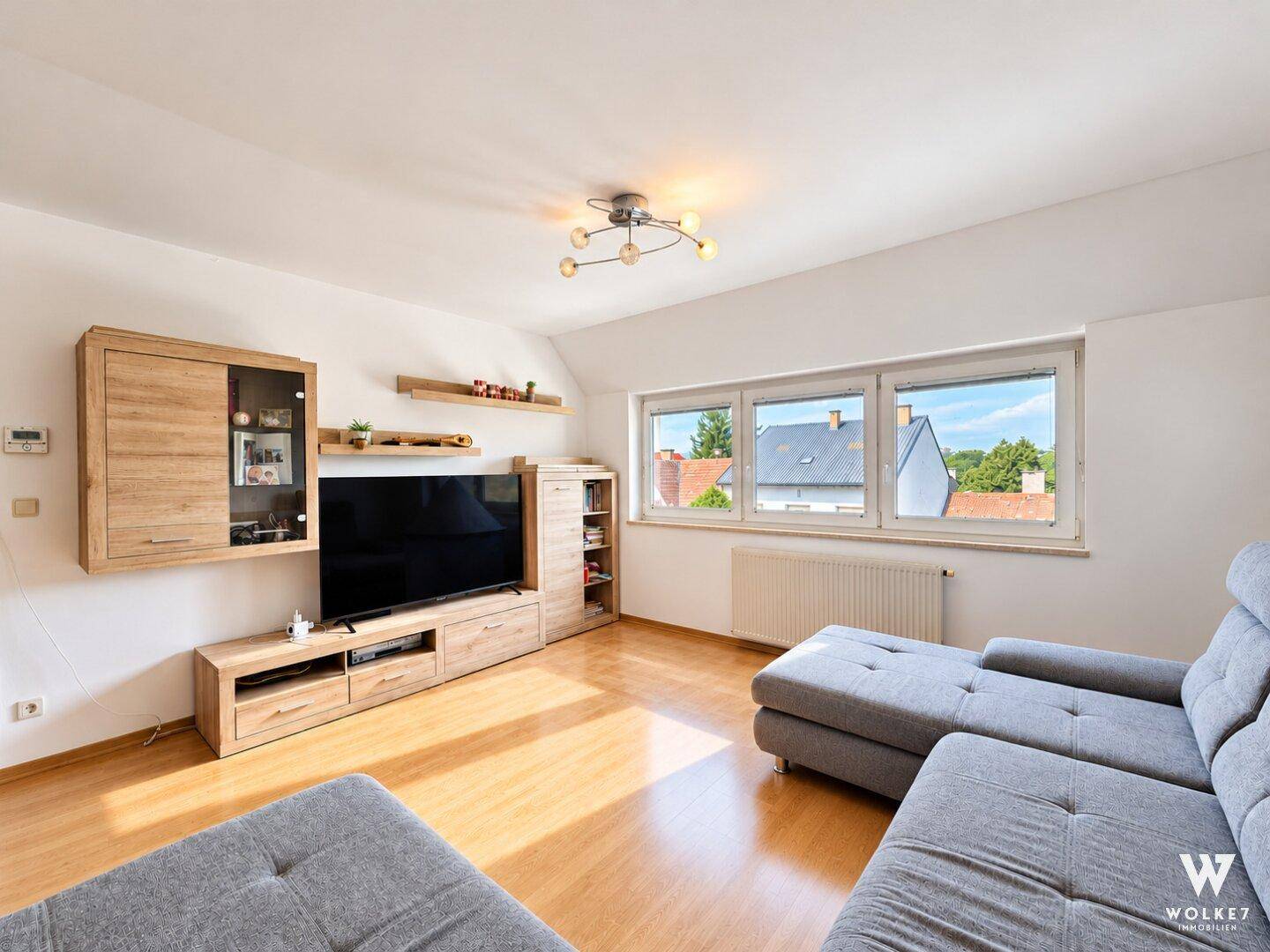 Geräumiges Wohnzimmer mit Laminatboden, großen Fenstern und Blick auf die Nachbarschaft.