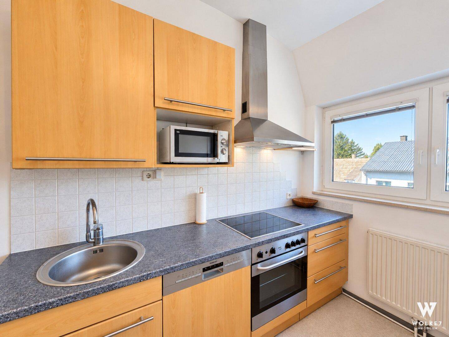 Detailansicht der Küche mit Spüle, Kochfeld, Backofen und Mikrowelle.