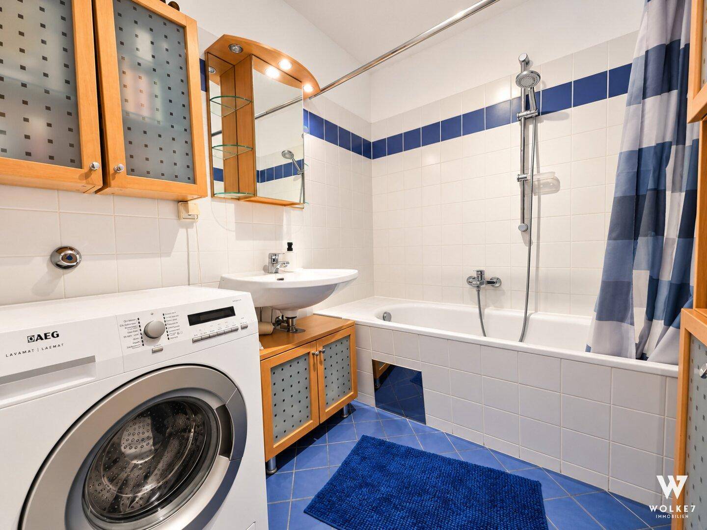 Badezimmer mit Badewanne, Waschbecken, Waschmaschine und blauen Fliesen.
