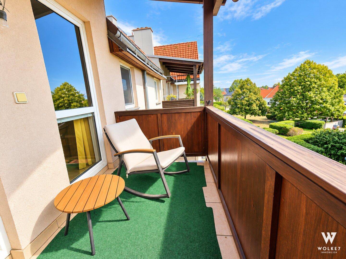 Gemütlicher Balkon mit Holzboden, Sitzgelegenheiten und Blick ins Grüne.