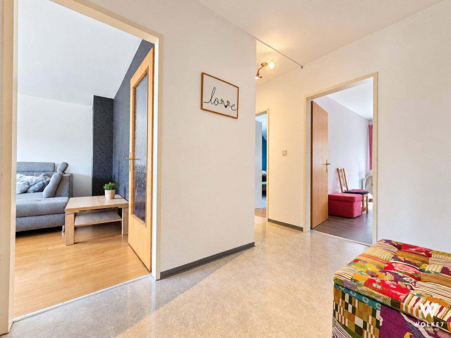 Heller Flur mit Zugang zu verschiedenen Räumen und modernem Sitzmöbel.
