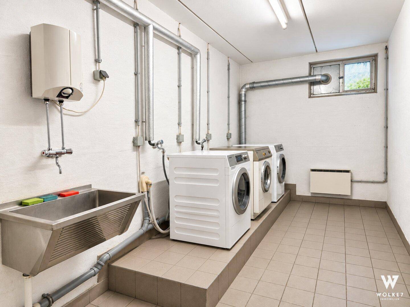 Gemeinschaftlicher Waschraum im Keller mit Waschmaschinen, Trocknern und Waschbecken.