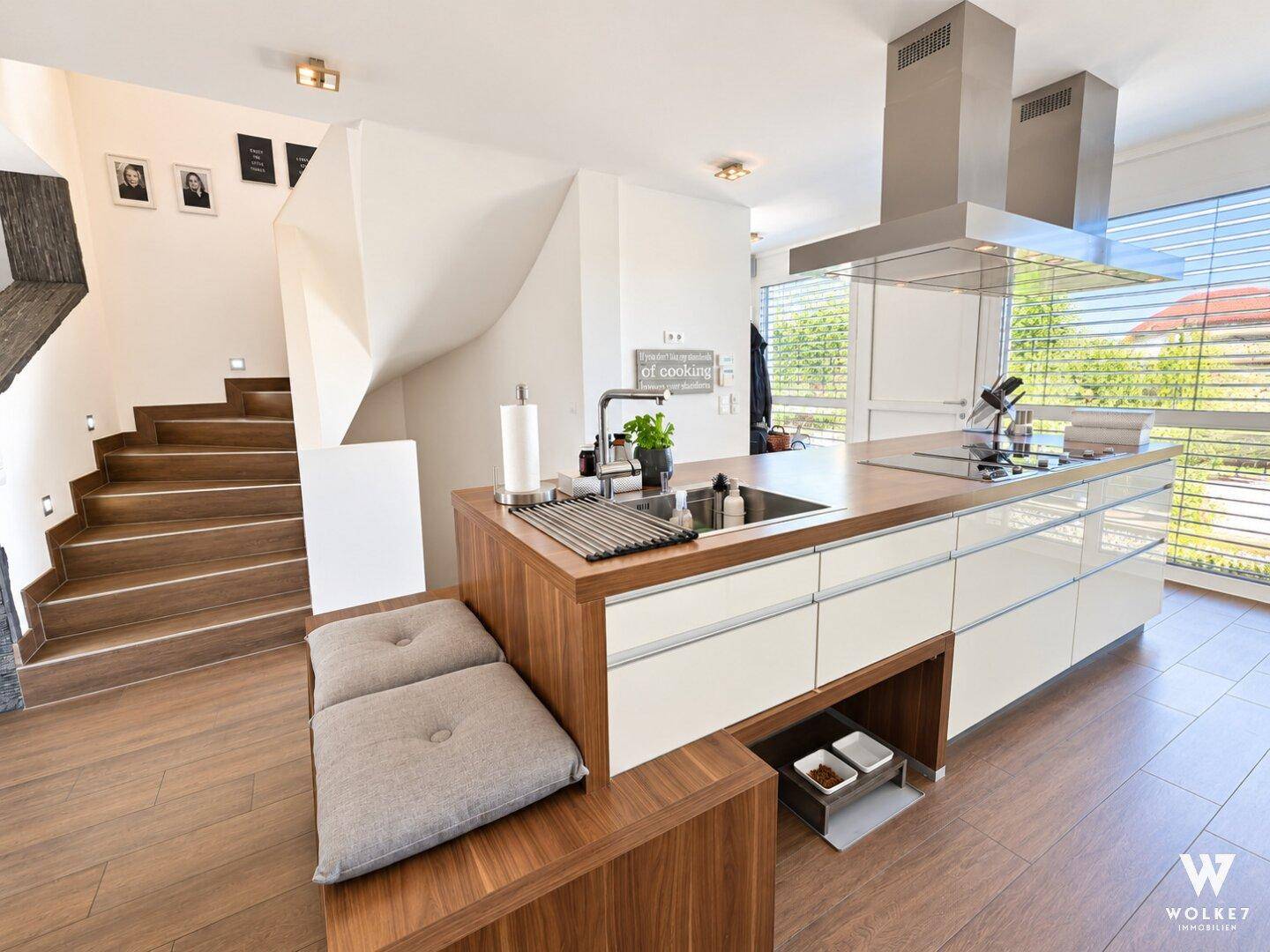 Helle Küche mit Kochinsel, Spülbecken und integrierter Sitzgelegenheit neben der Treppe.