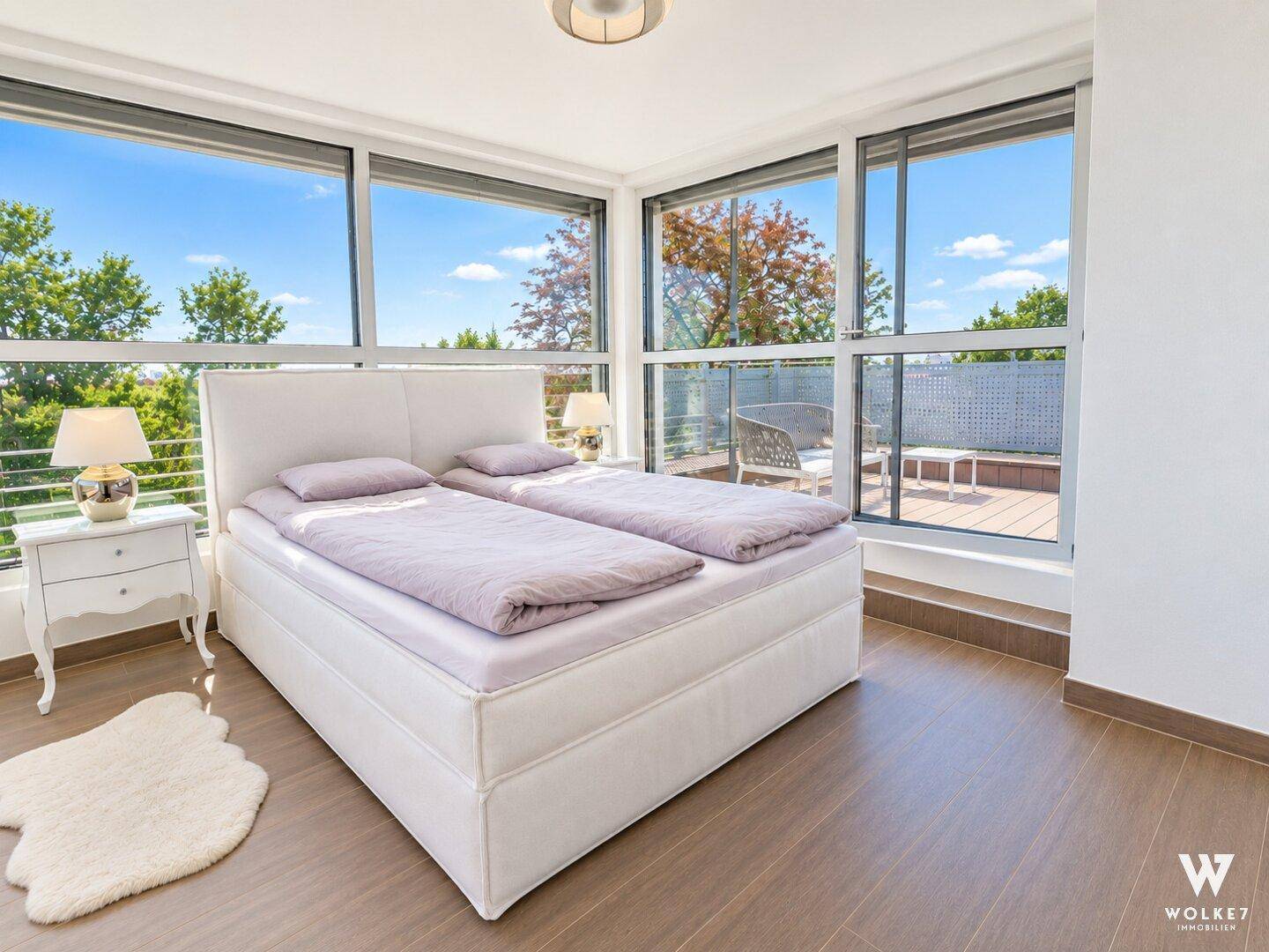 Helles Schlafzimmer mit großen Fenstern, Holzboden und Zugang zur Terrasse.