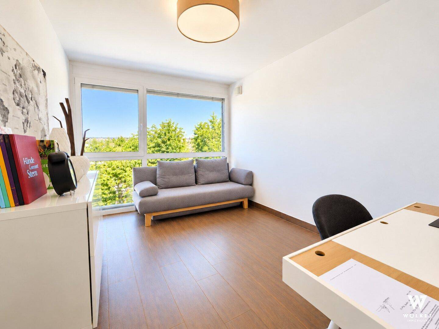 Helles Arbeitszimmer mit großem Fenster, Holzboden und Blick ins Grüne.