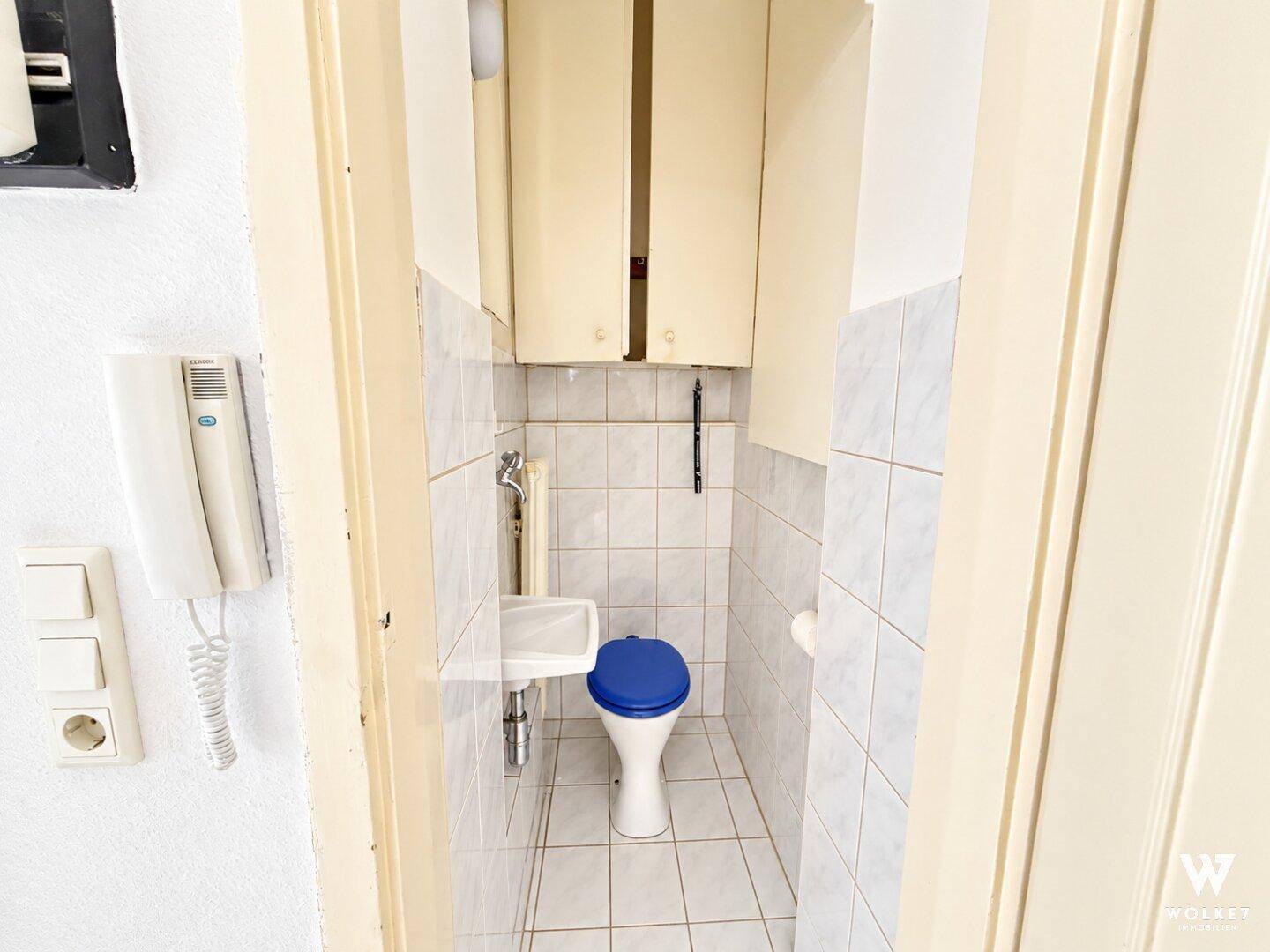 Kleines Gäste-WC mit weißen Fliesen, einem Waschbecken und praktischen Oberschränken.