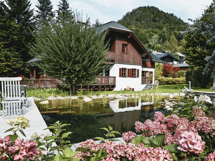 Charmantes Haus mit Holzfassade, umgeben von einem blühenden Garten und einem natürlichen Schwimmteich.