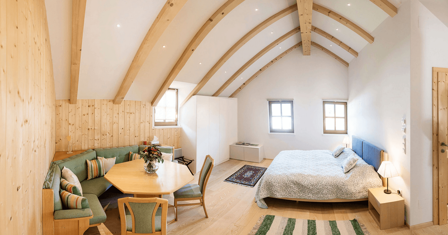 Helles Schlafzimmer im Dachgeschoss mit Holzbalken, gemütlicher Sitzecke und Holzwänden.