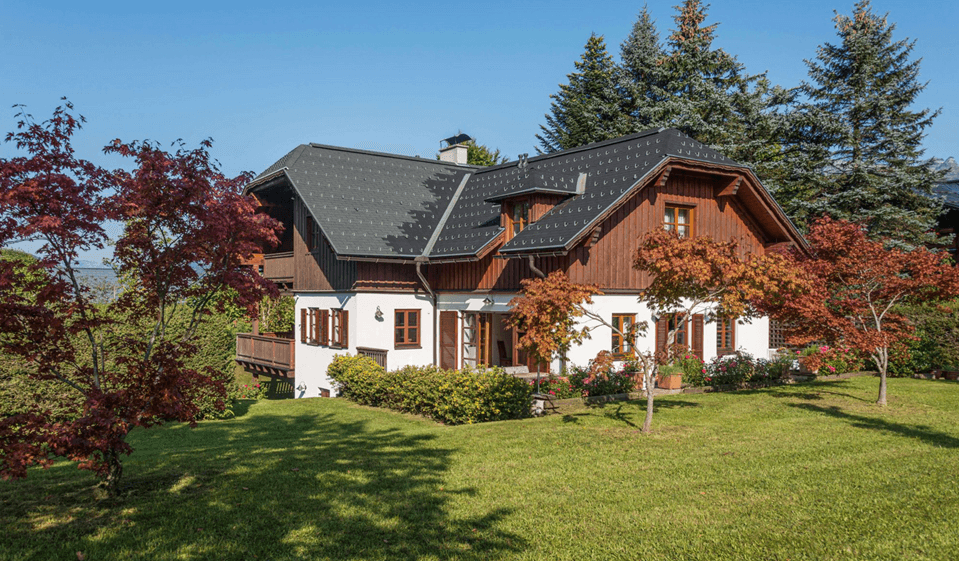 Attraktives Landhaus mit weißer Fassade, Holzverkleidung und gepflegtem Vorgarten unter blauem Himmel.