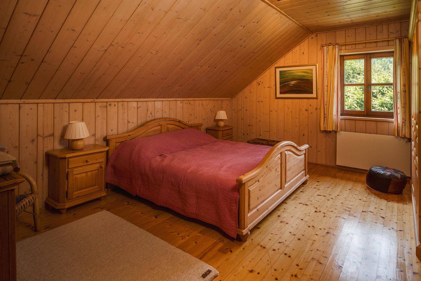 Rustikales Schlafzimmer mit Holzvertäfelung, Holzboden und schräger Decke im Dachgeschoss.