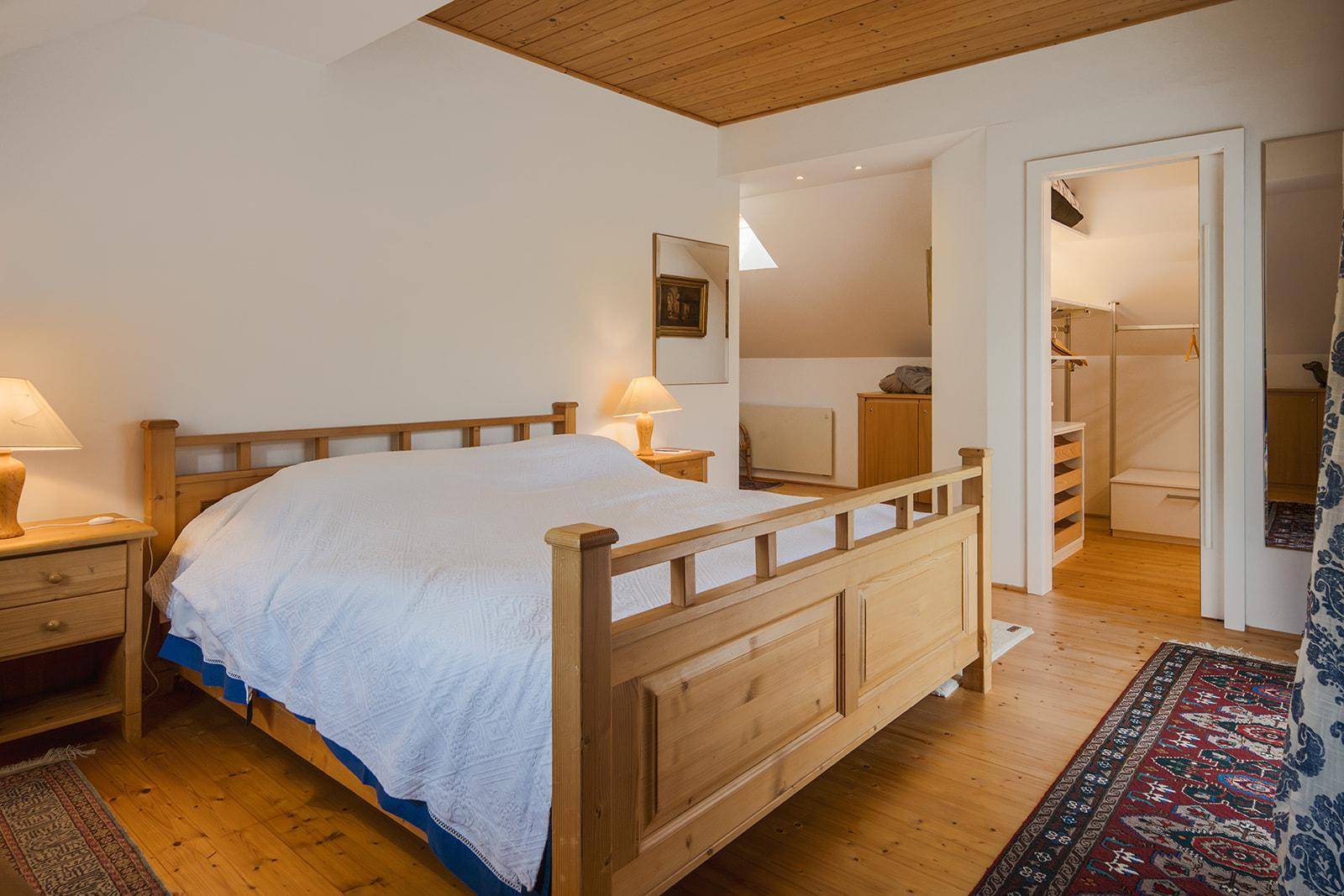 Helles Schlafzimmer mit Holzdoppelbett, Parkettboden und Zugang zu einem begehbaren Kleiderschrank.