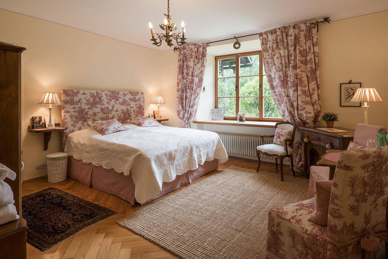 Charmantes Schlafzimmer mit traditionellem Dekor, Holzboden und Blick ins Grüne durch das Fenster.