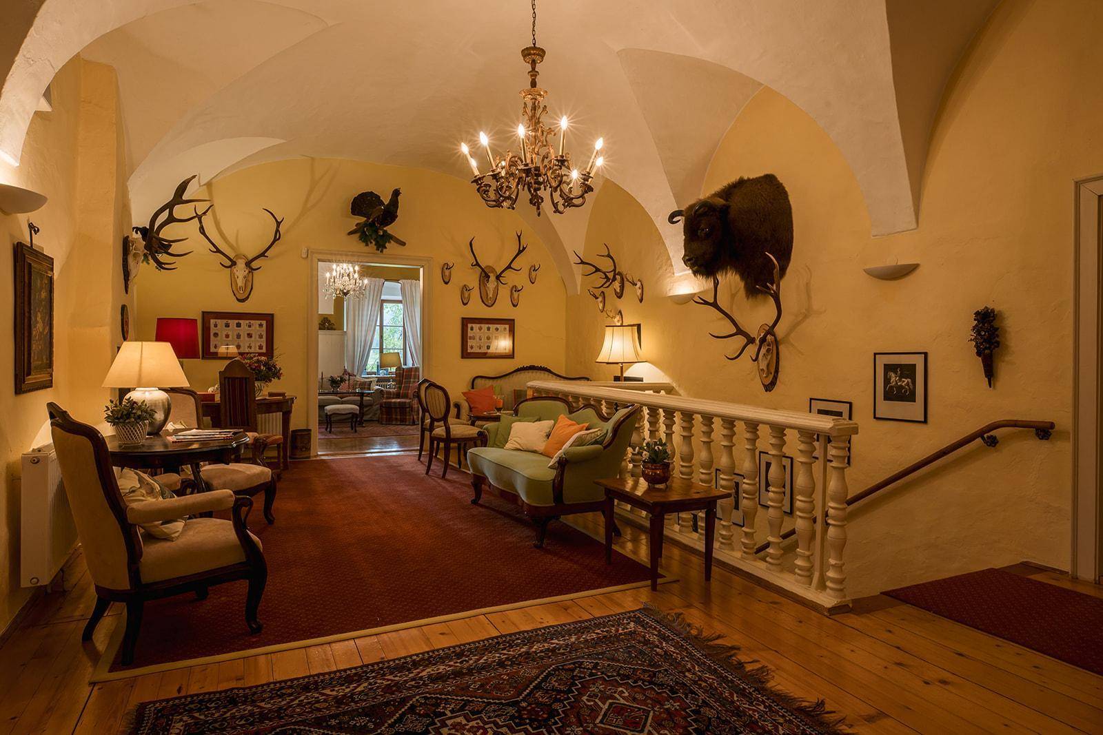 Geräumige Diele mit Gewölbedecke, Holztreppe und traditioneller Einrichtung mit Jagdtrophäen.
