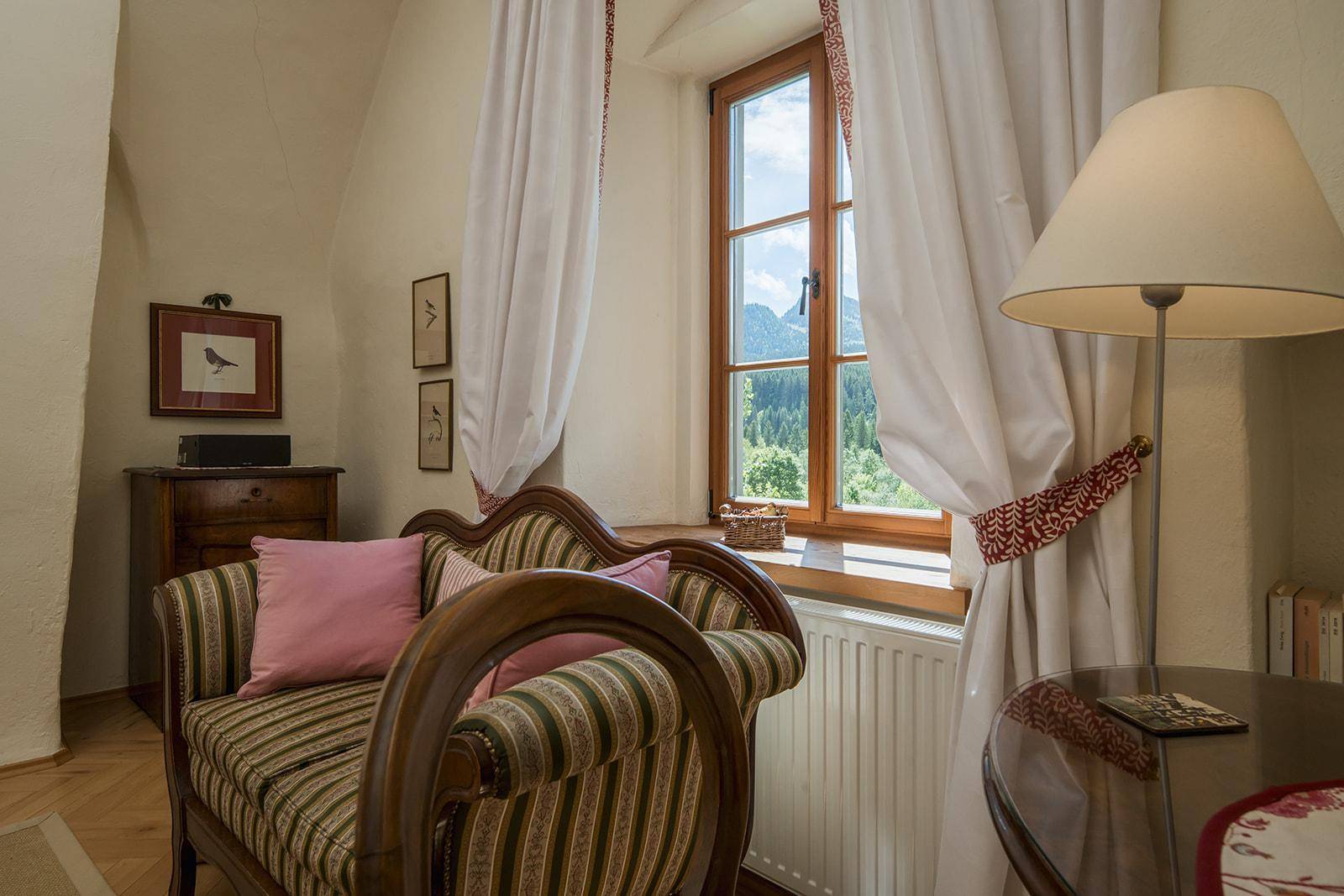 Gemütlicher Sitzbereich mit traditionellem Sofa, Holzboden und Blick auf die Berge durch das Fenster.