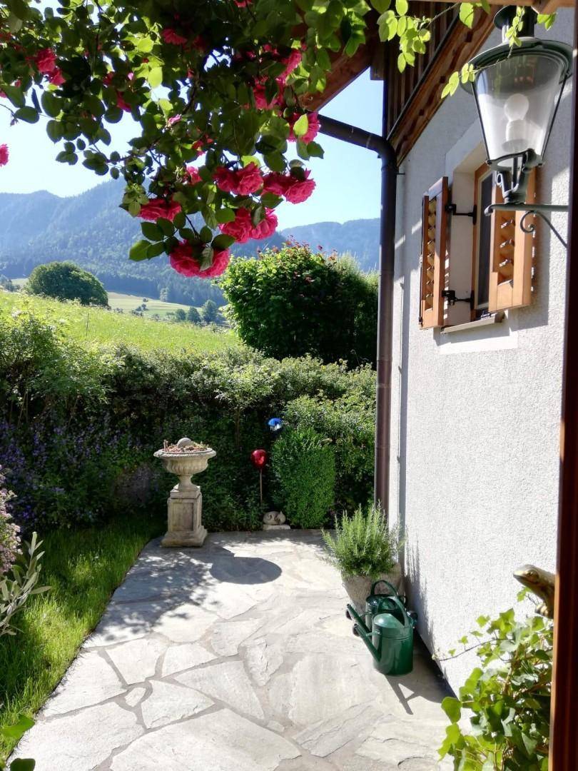 Idyllischer Gartenweg mit blühenden Rosen, einer Steinvase und Blick auf die grüne Landschaft.