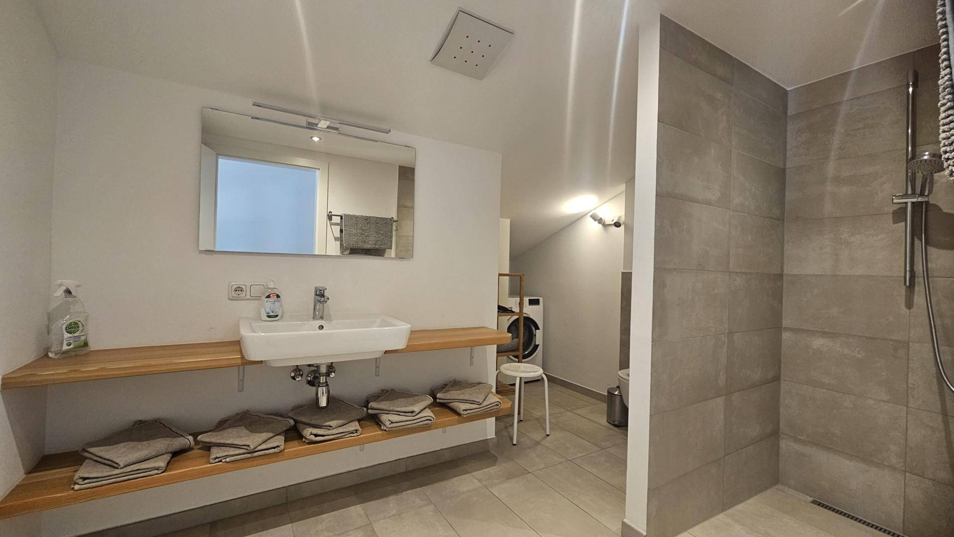 Modernes Badezimmer mit begehbarer Dusche, Einzelwaschbecken und Waschmaschine.