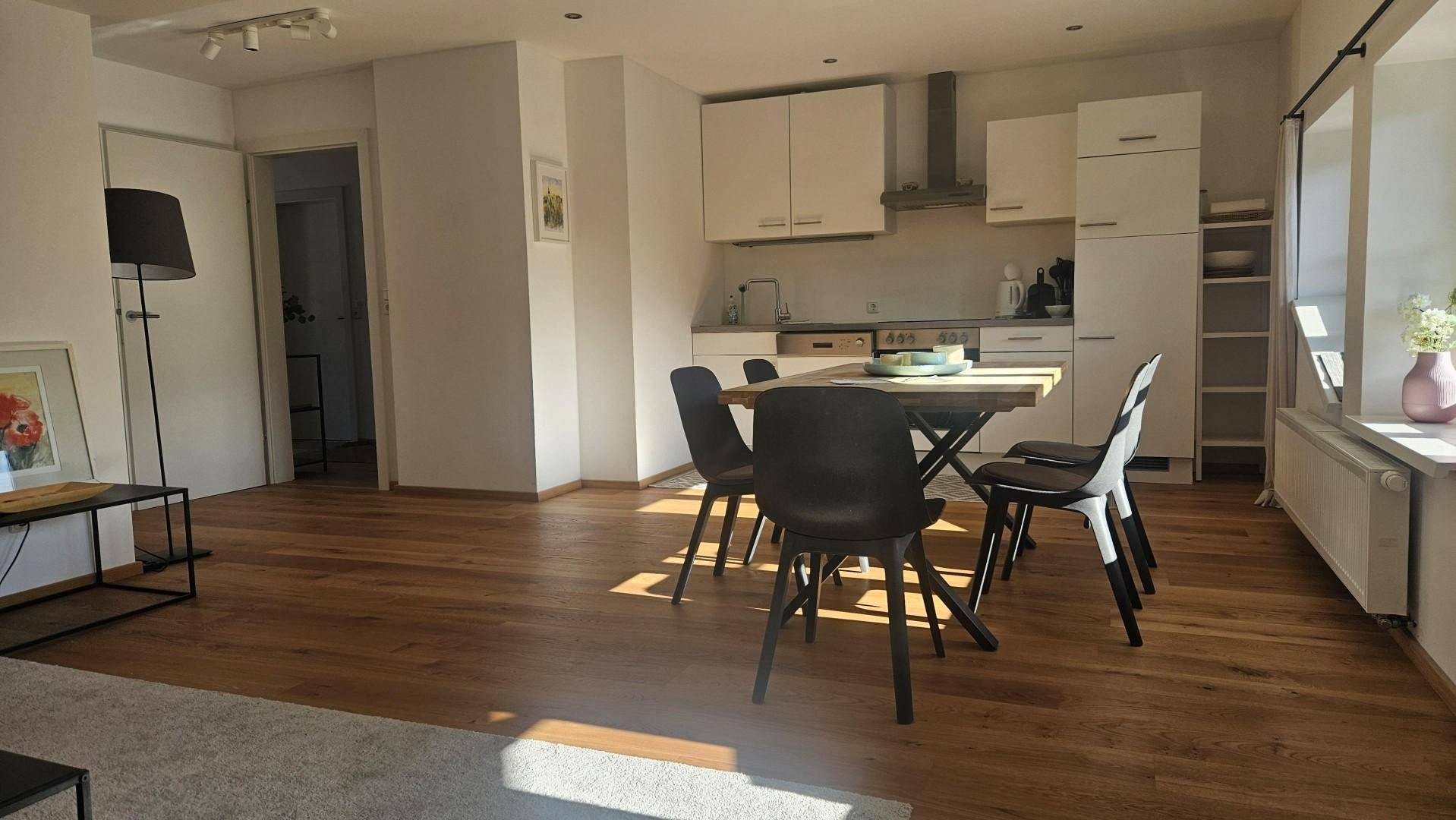 Moderne, offene Küche mit weißen Schränken und Essbereich, gut beleuchtet.