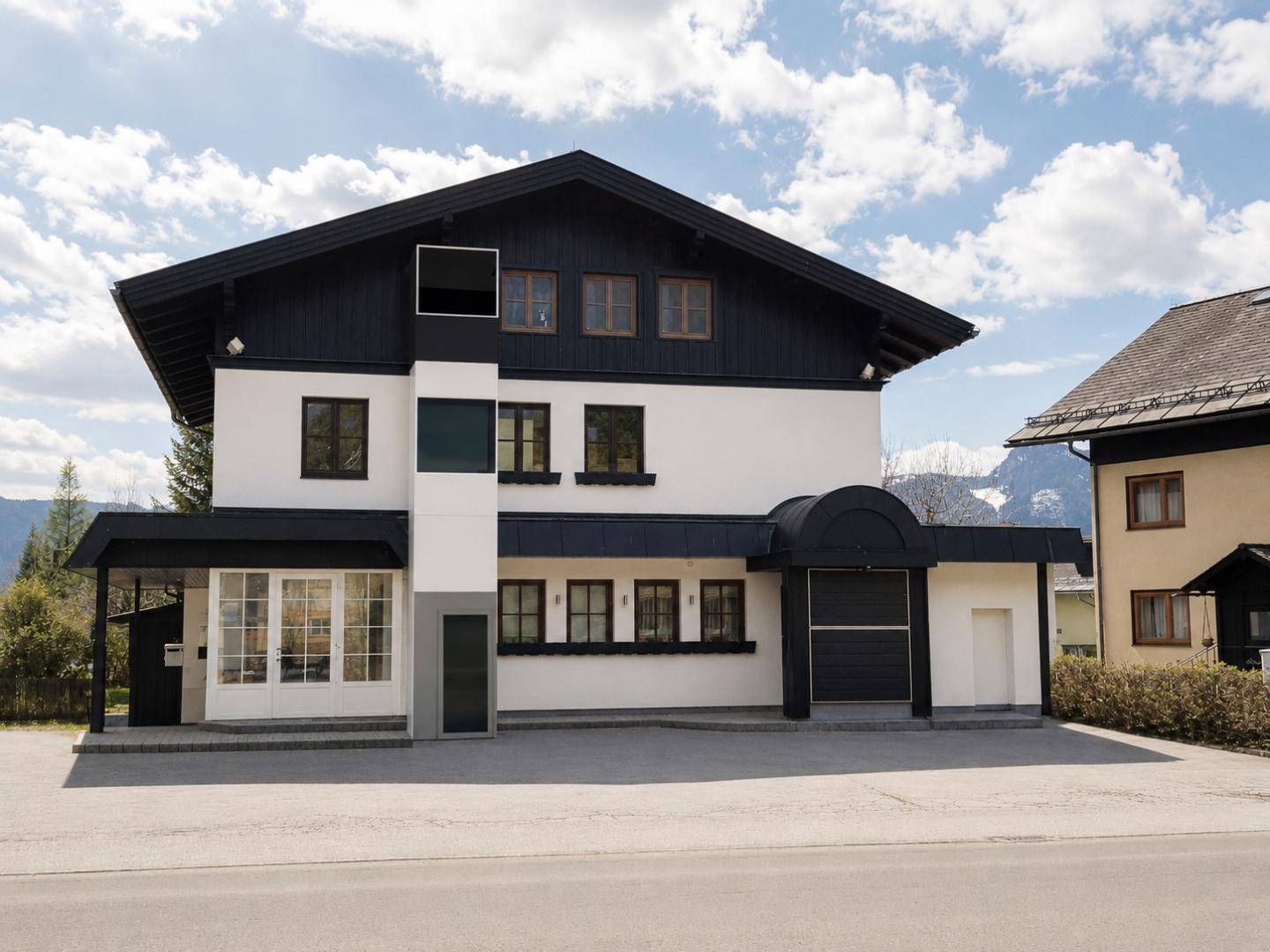 Traditionelles Haus mit schwarzem Dach, weißer Fassade und Bergblick in ländlicher Umgebung.