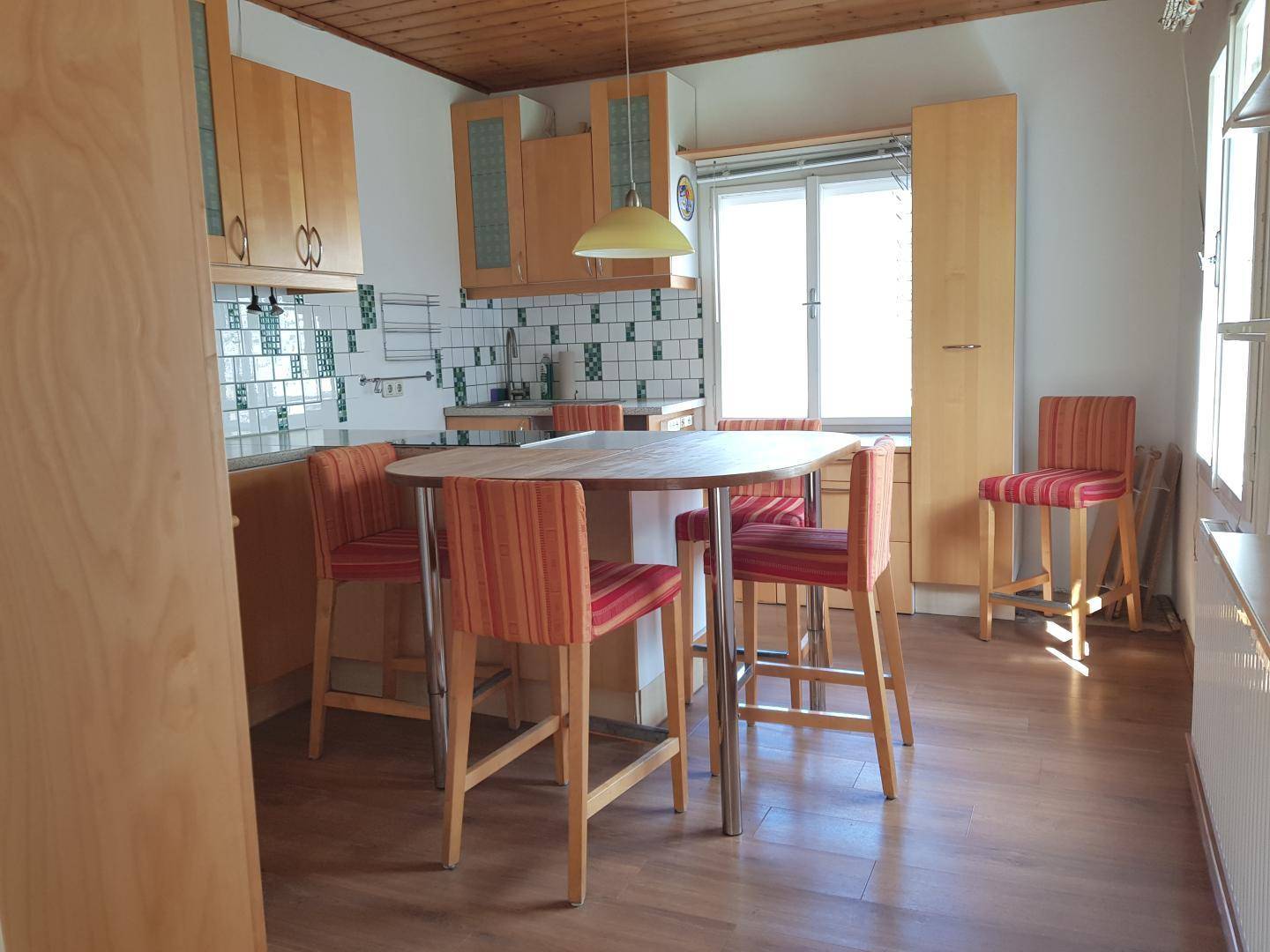 Funktionale Küche mit Holzelementen, Essbereich und Blick ins Grüne durch das Fenster.