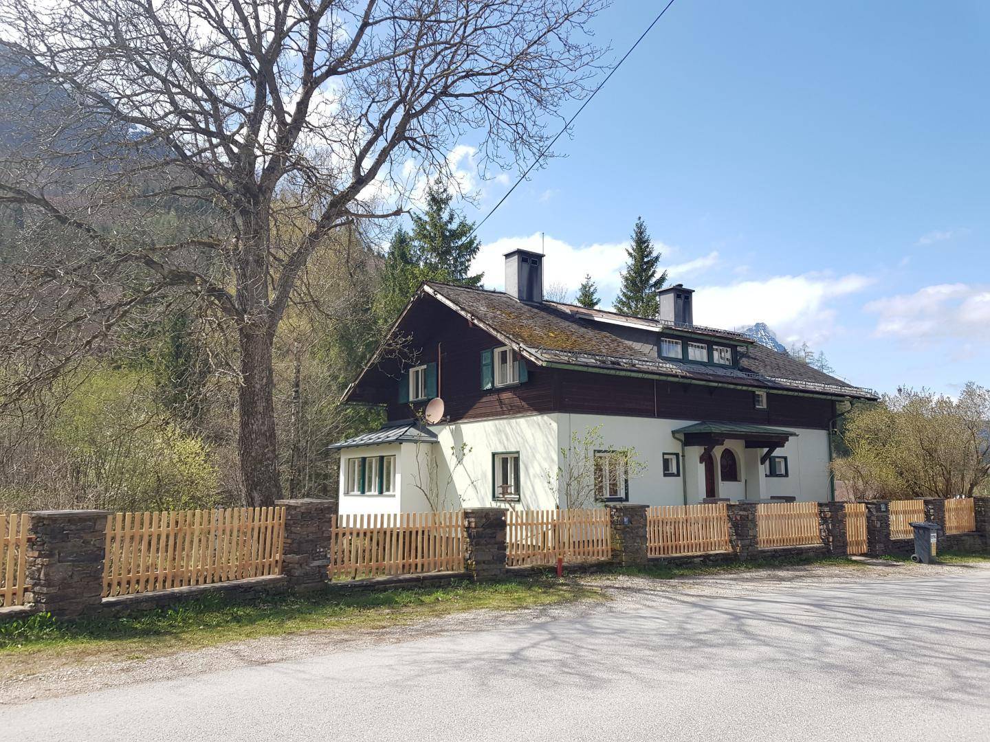 Charmantes Haus mit traditioneller Architektur, Holzzaun und Blick auf die umliegende Berglandschaft.