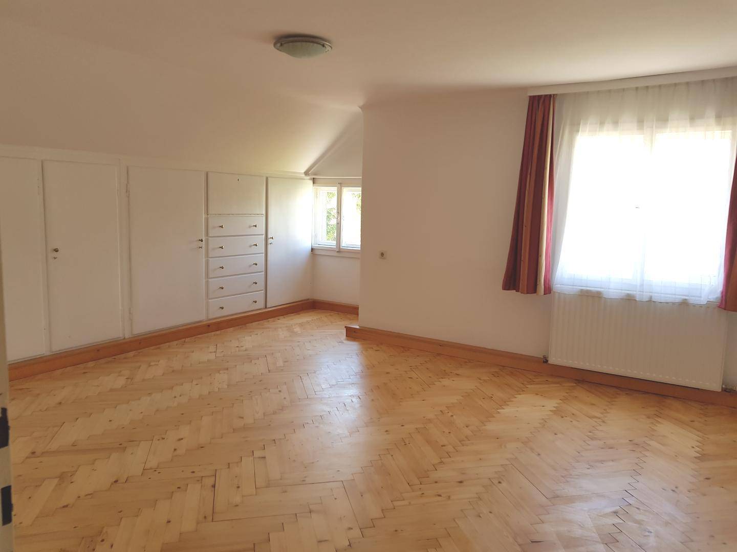 Helles Schlafzimmer im Dachgeschoss mit Einbauschränken, Holzboden und schrägen Decken.
