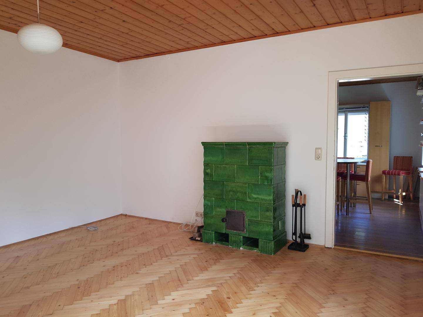 Gemütliches Wohnzimmer mit traditionellem Kachelofen, Fischgrätparkett und Holzbalkendecke.