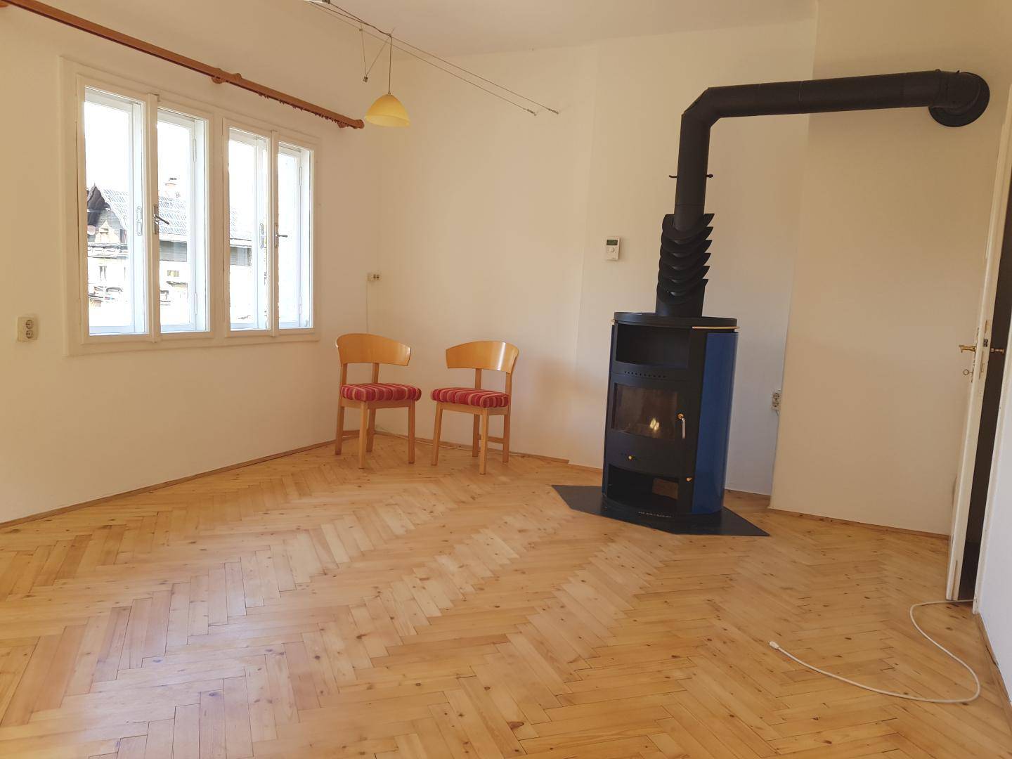 Helles Wohnzimmer mit Fischgrätparkett, einem modernen Kaminofen und großen Fenstern.