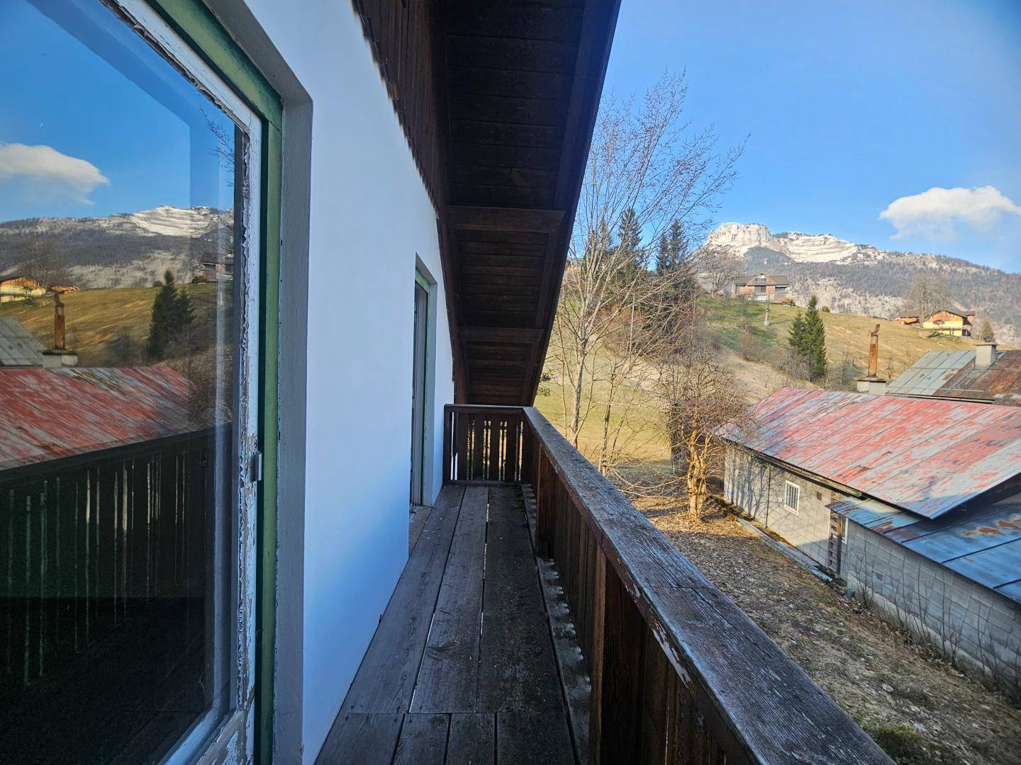 Blick vom Holzbalkon auf eine malerische Berglandschaft und die Dächer der umliegenden Häuser.