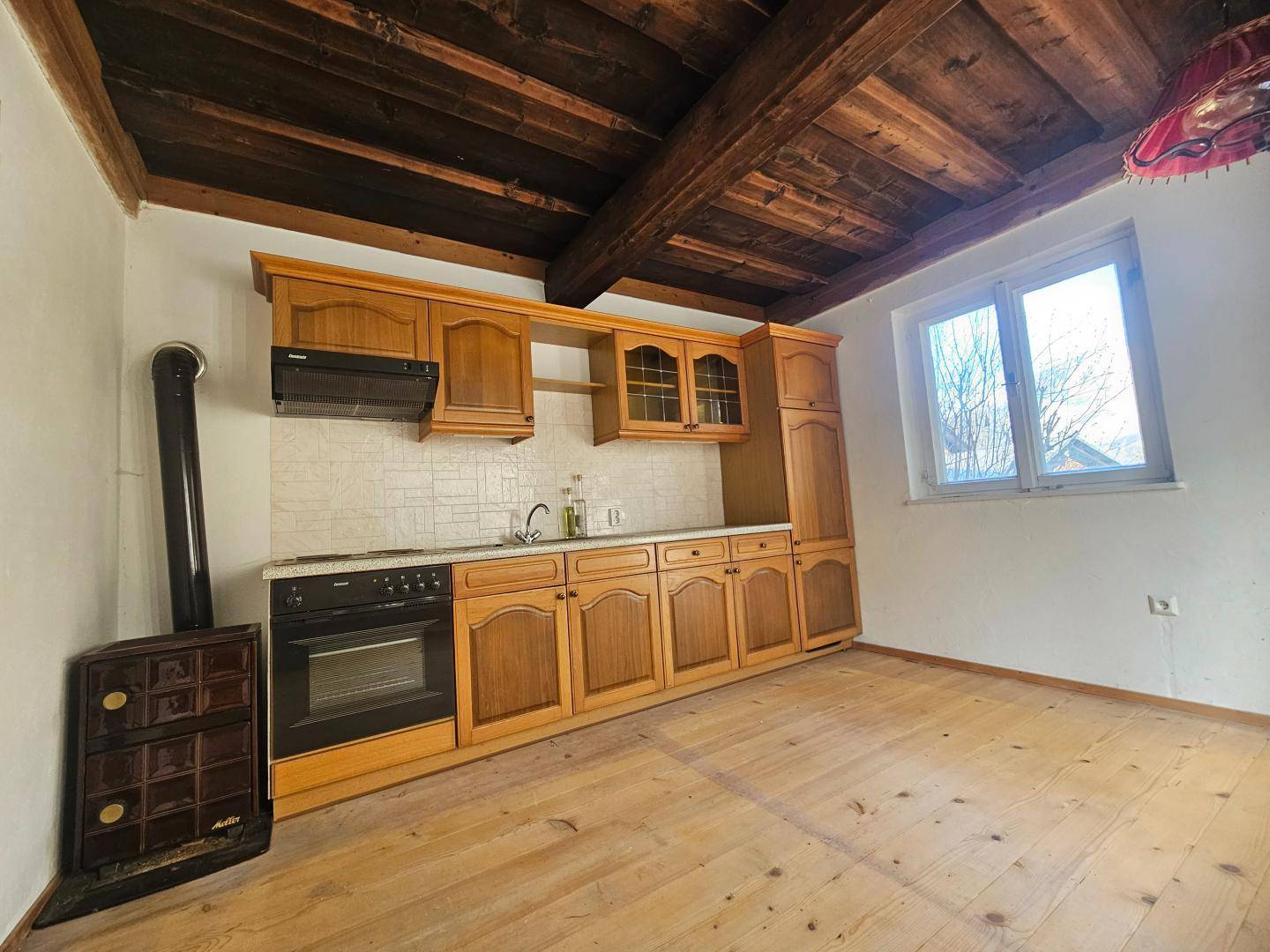 Rustikale Küche mit Holzbalkendecke, Einbauküche und traditionellem Holzofen.