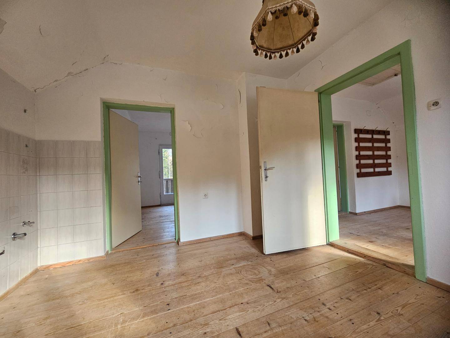 Leerer Raum mit Holzdielenboden, weißen Wänden und grünen Türrahmen, bereit zur Renovierung.