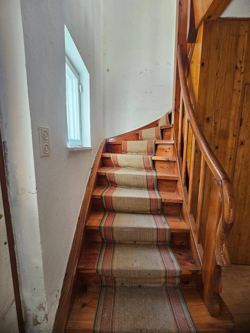 Rustikale Holztreppe mit Teppichläufer und kleinem Fenster, die in die obere Etage führt.