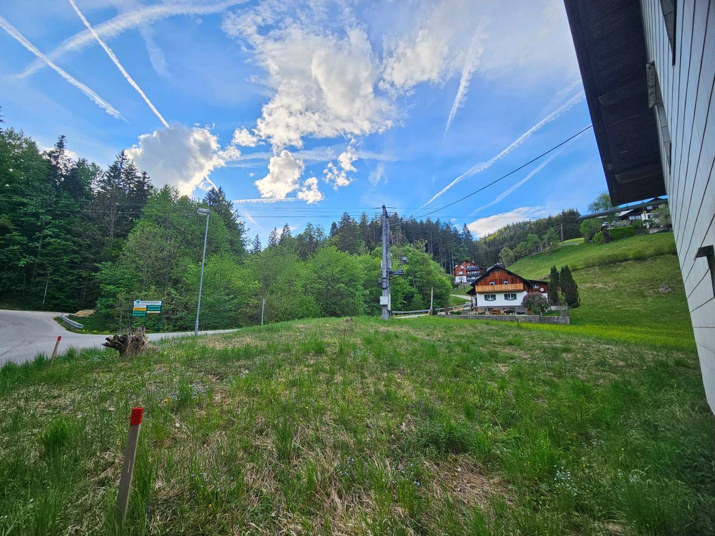 Weitläufige Grünfläche mit Bäumen und Häusern in der Ferne unter einem weiten Himmel.