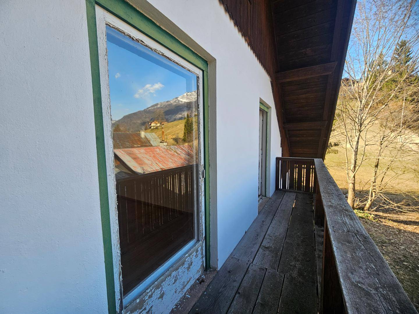 Detailansicht des Holzbalkons mit Blick durch das Fenster auf die umliegende Bergwelt.