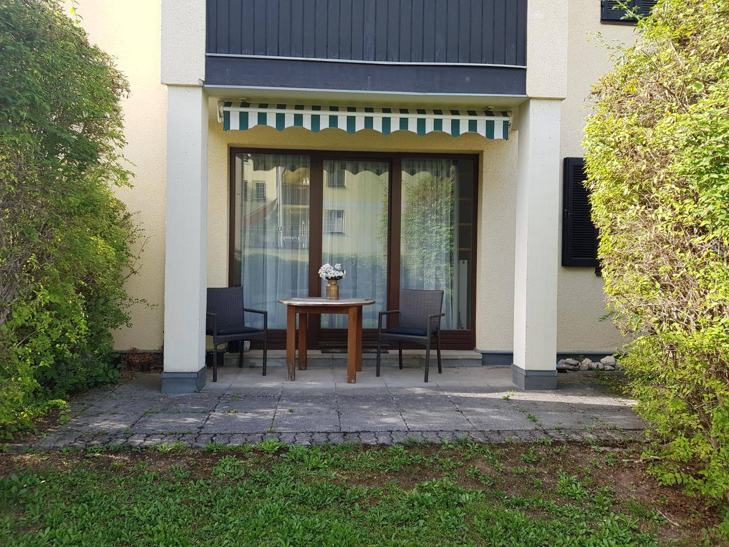 Gemütliche Terrasse im Erdgeschoss mit Gartenmöbeln, Markise und direktem Zugang zum Rasen.